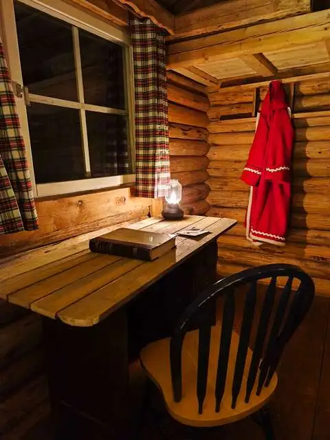 Intérieur chaleureux d'une cabane en bois à Santa Forest près de Rovaniemi, éclairée à la lampe à huile avec vue sur les sapins enneigés, où l'on attend le Père Noël.